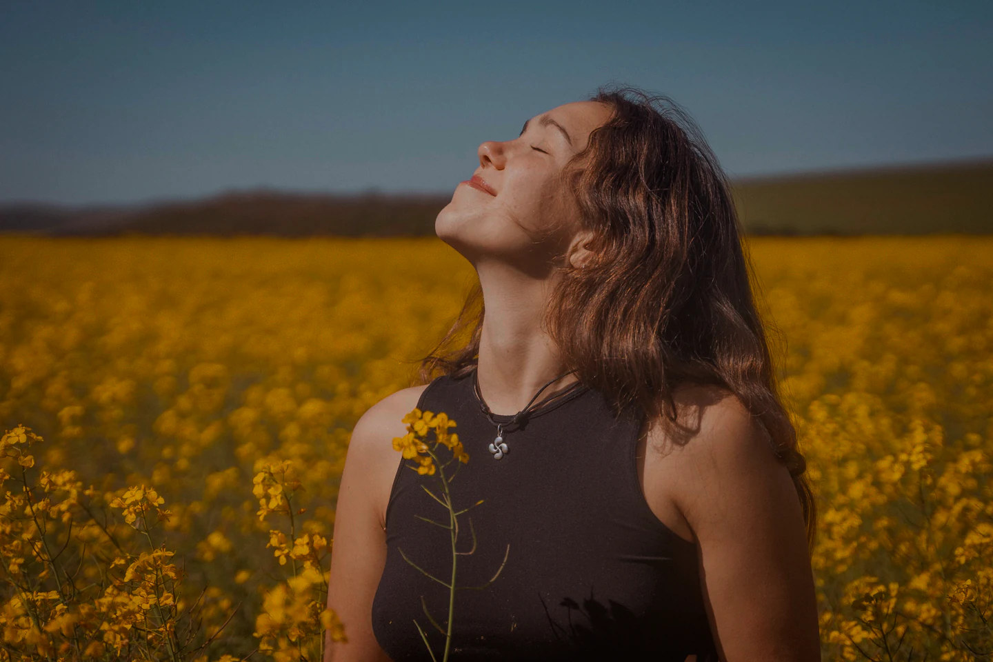 A young woman standing in a field of yellow flowers, face turned up to the sun
