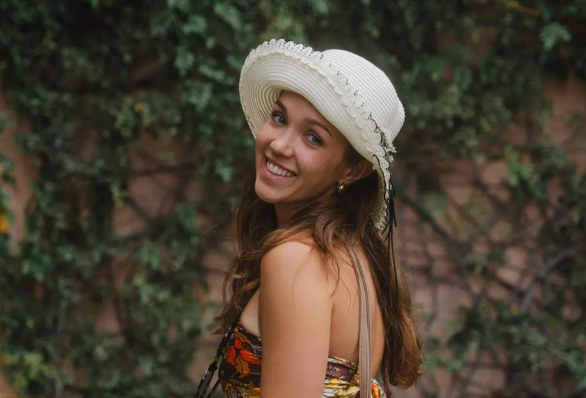 Kirsty Tornare smiling in a white sun hat in front of a leafy wall