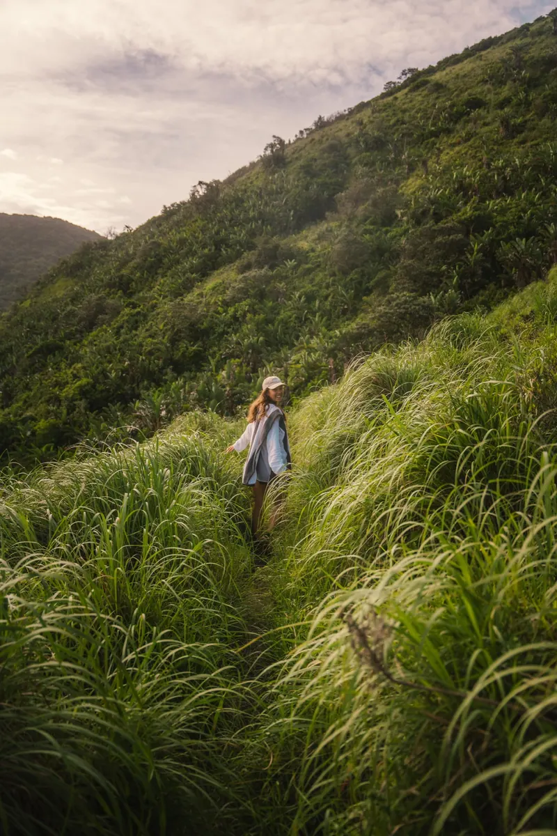 A woman on a narrow trail through tall grass on a hillside